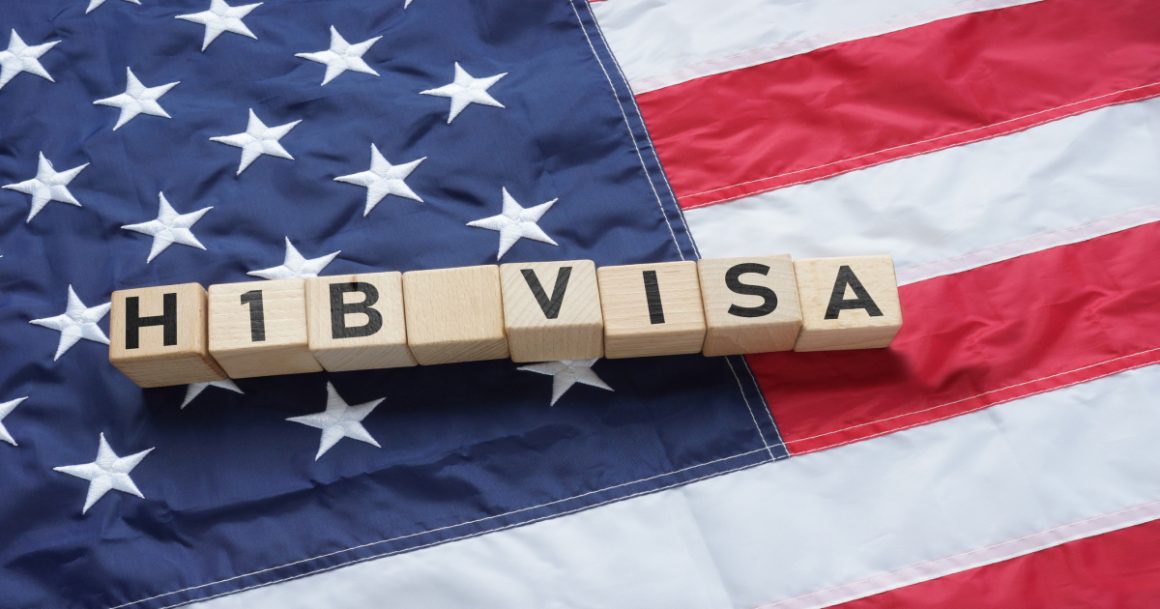 Wooden letter blocks spelling "H1B VISA" placed on an American flag, representing H-1B visa sponsorship opportunities in the United States.