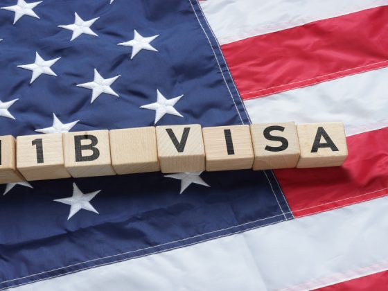 Wooden letter blocks spelling "H1B VISA" placed on an American flag, representing H-1B visa sponsorship opportunities in the United States.