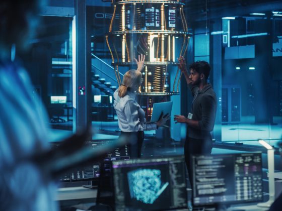 Two quantum computing engineers discussing research in front of a large quantum processor in a high-tech laboratory