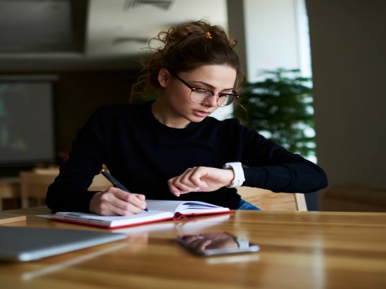 A focused young professional wearing a smartwatch to track time while planning tasks in a notebook
