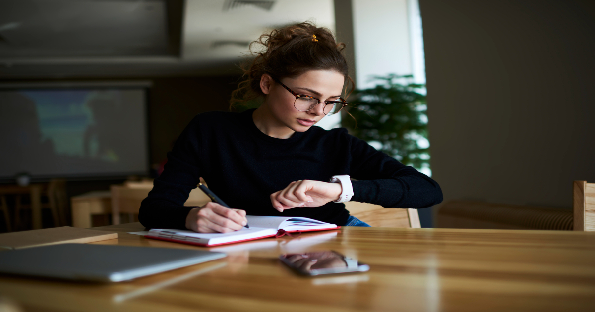 A focused young professional wearing a smartwatch to track time while planning tasks in a notebook