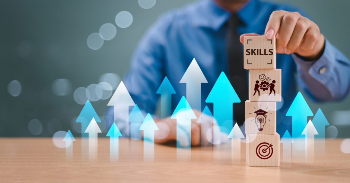 A professional in a blue shirt stacks wooden blocks labeled with icons for skills, teamwork, learning, and goal-setting, surrounded by upward-pointing blue and white arrows symbolizing career growth.