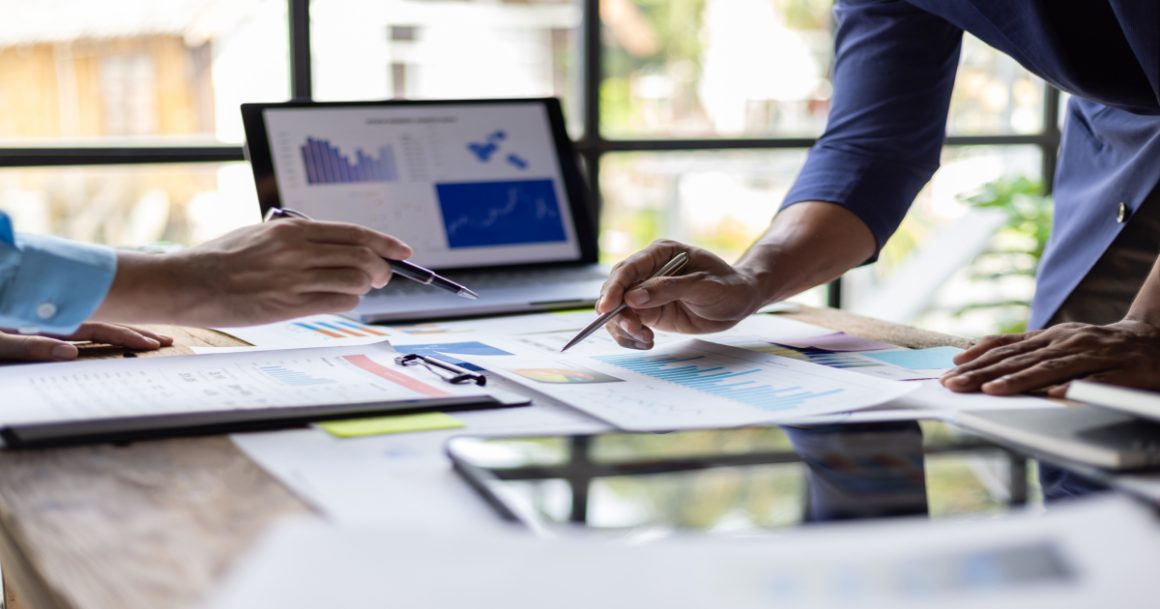 Two people analyzing market data charts and reports at a desk during a business meeting.