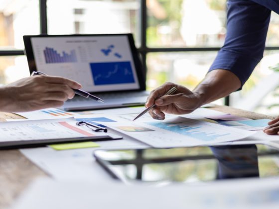 Two people analyzing market data charts and reports at a desk during a business meeting.