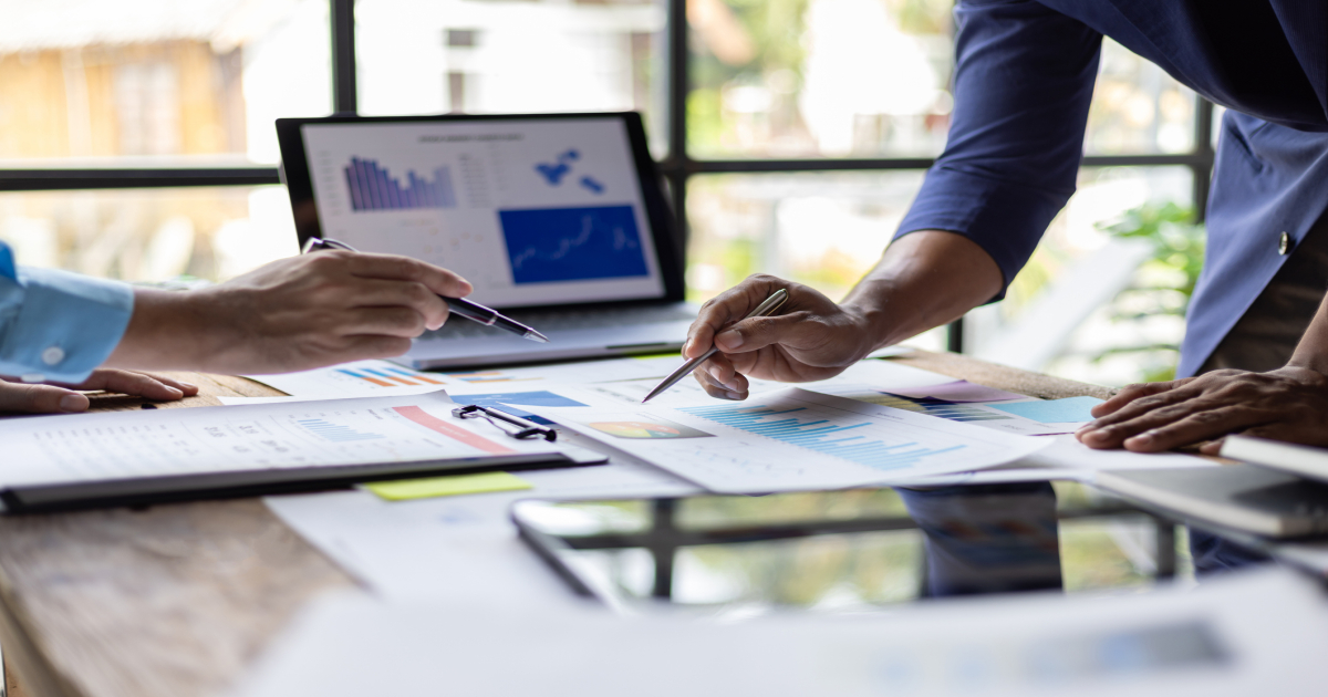 Two people analyzing market data charts and reports at a desk during a business meeting.