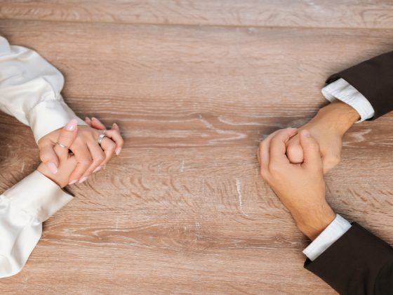 Two people with clasped hands facing each other across a table, illustrating workplace conflict resolution.