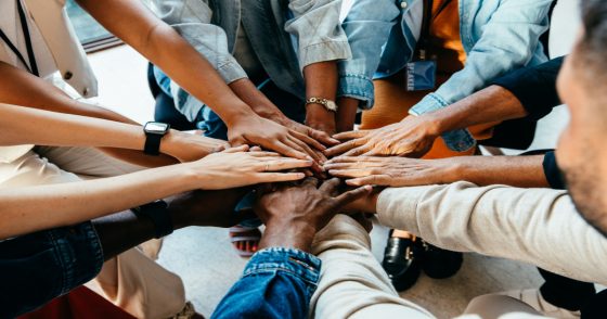Diverse team stacking hands together in a circle to show teamwork and collaboration.
