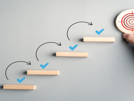 Ascending wooden blocks with checkmarks leading to a bullseye, illustrating goal-setting techniques and step-by-step progress.