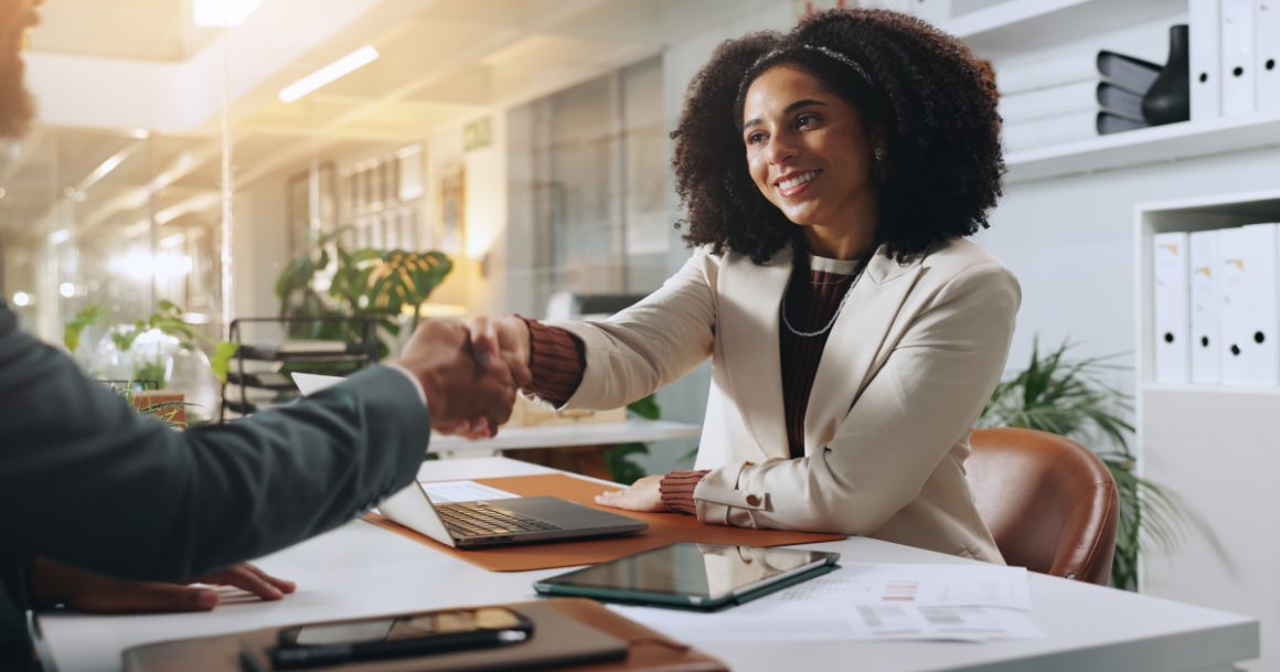 Job candidate and hiring manager shaking hands across a desk while discussing multiple job offers
