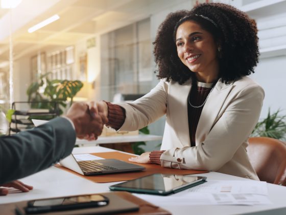 Job candidate and hiring manager shaking hands across a desk while discussing multiple job offers