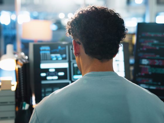 Backend developer writing code on multiple monitors in a dark office.